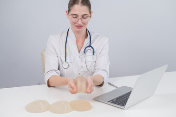 Woman plastic surgeon demonstrating breast implants at her desk. 