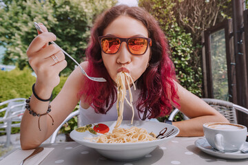 The girl is in a funny hurry and eats Italian pasta in a cafe. The concept of good manners and...