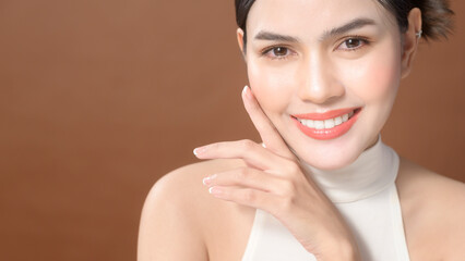 A young woman with beautiful face smiling , touching her face over brown background , beauty skin care concept