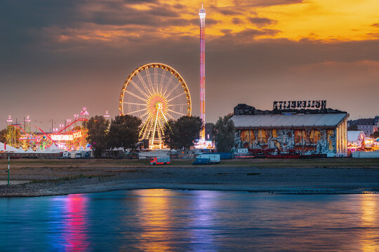 22 July 2022, Dusseldorf, Germany: Evening View Of Fair Festival And Amusement Park At A Traditional Festival On The Bank Of The Rhine River. Ferris Wheel And Other Illuminated Attractions