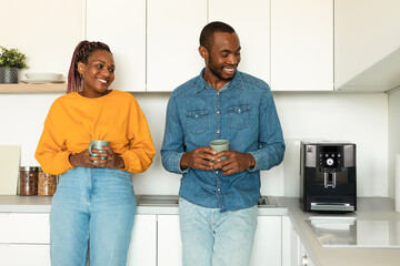 Excited african american spouses drinking coffee in kitchen, looking at modern coffee machine and...