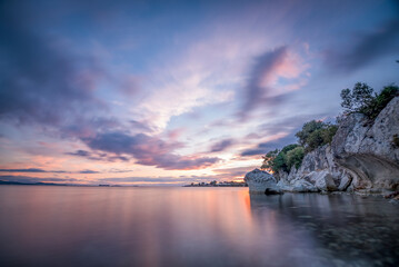 Obraz na płótnie Canvas Sunset with rocks, Rock on sea with colorful sunset clouds beautiful background for travel agencies