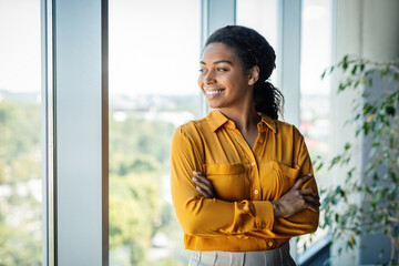 Portrait of confident african american businesswoman standing near window in modern company office, free space