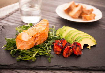 dish of cooked salmon fillet with fresh vegetables and herbs on a black stone plate