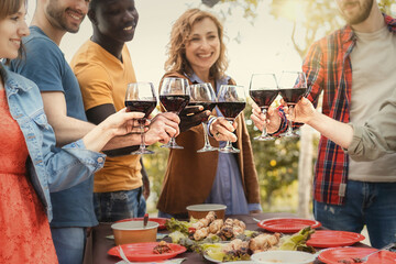Cheerful Family drinking red wine and cheering outside - Best friends toasting together during the...