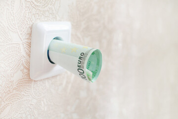 The concept of expensive energy and electricity cost. Euro banknotes in a white electrical socket. Energy saving.