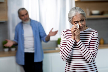 Depressed Senior Woman Crying In Kitchen During Argue With Husband
