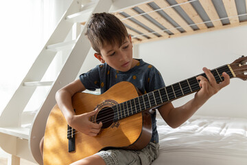 Boy learning to play acoustic guitar. Boy is practicing acoustic guitar in his room