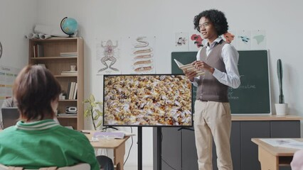 Medium long low angle of Black guy making presentation to classmates, showing educational video about bees