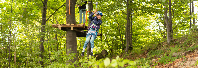 Little girl preschooler wearing full climbing harness having fun time in the rope park using carabiner and other safety equipment. Summer camp activity for kids. Adventure park in the forest