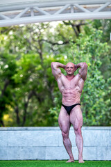 White man on stage with green grass demonstrates a beautiful male body with tensed muscles