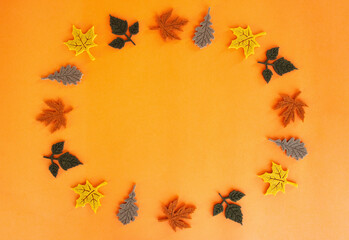Beautiful autumn flat lay of felt decoration leaves of oak and maple of yellow red orange green and brown colors standing in a circle and spinning around its axis on orange background.