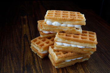 Delicious fresh Viennese waffles with white cream lie on a wooden table.