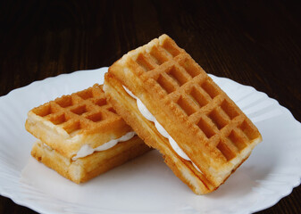 Fresh Viennese waffles with white cream on a white plate.