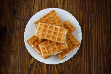 A pile of ruddy Viennese waffles lie on a white plate on a wooden background.