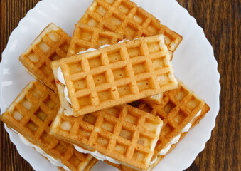 A pile of ruddy Viennese waffles lie on a white plate on a wooden background.