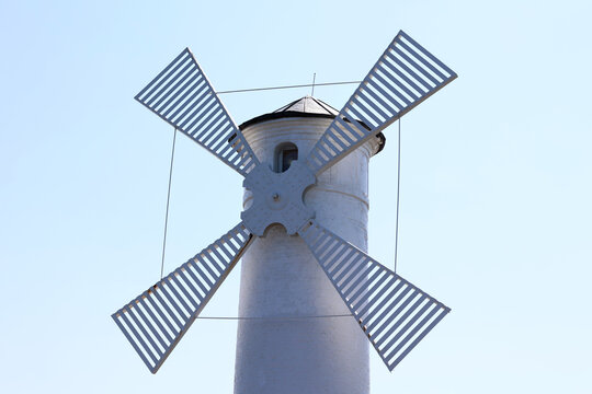 Biały wiatrak nad morzem na tle niebieskiego nieba w słońcu. 