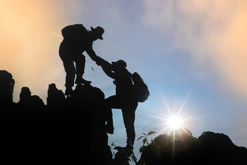 Silhouette of hiker helping each other hike up a mountain at sunset. - obrazy, fototapety, plakaty