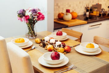 Fall table setting for celebration Thanksgiving day family party. Autumn composition with candles, fruits, nuts and cones. Plates with pumpkins and pomegranate. Natural autumn decor. Selective focus