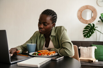 Young beautiful focused african woman working with laptop during lunch