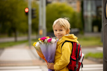 Fototapeta premium Cute preschool child, waiting on a red light to cross the street, caring bouquets of flowers for teachers, going to preschool