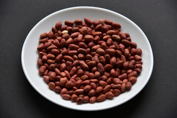Peanuts on a white plate on a black background. Delicious nutty breakfast.