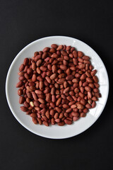 Peanuts on a white plate on a black background. Delicious nutty breakfast.