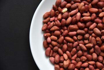 Peanuts on a white plate on a black background. Delicious nutty breakfast.