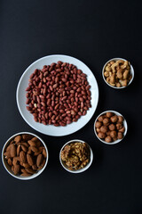 Peanuts on a white plate on a black background. Delicious walnut breakfast with walnuts, cashews and almonds.