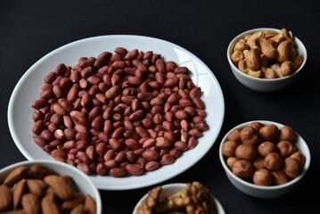 Peanuts on a white plate on a black background. Delicious walnut breakfast with walnuts, cashews and almonds.
