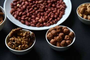 Peanuts on a white plate on a black background. Delicious walnut breakfast with walnuts, cashews and almonds.