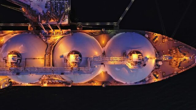 Aerial top down of Liquified Natural Gas LNG carrier moored to a small gas terminal at night. Fuel crisis. Sanctions