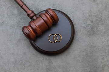 Law theme. Judge gavel wedding rings on concrete stone grey background. Divorce proceedings. Mallet...
