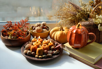 Pumpkin shape cup, nuts, pumpkin, decorative candles, books, dry grass on windowsill. Autumn...