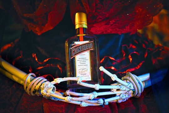 Minsk, Belarus. Oct 2021. Female skeleton hands hold bottle of liqueur Cointreau. Halloween holiday decoration.