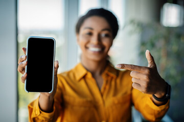 Great offer. Black businesswoman holding and pointing finger at cellphone with empty screen, promoting app or website
