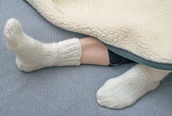 Women's feet in white wool socks on a gray knitted blanket. Autumn concept. 