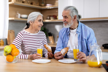 Portrait Of Cheerful Elderly Couple Having Breakfast Together In Kitchen Interior