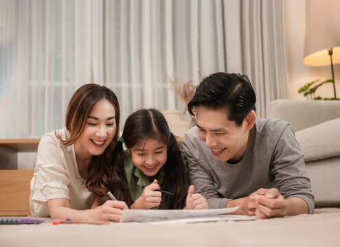 Happy Asian Family Father, Mother, And Daughter Relaxing By Playing And Painting Together On Carpet In The Living Room At Home.