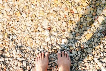 Feet on a pebbly beach at the water's edge