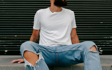 Young bearded hipster guy wearing white blank t-shirt and blue jeans in a random urban style....