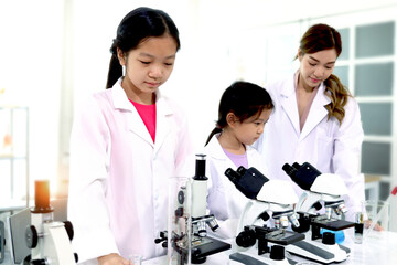 Students and teacher in lab coat have fun together while learn science experiment in laboratory. Young adorable Asian scientist kid using microscope, apparatus and lab equipment for research. Science 