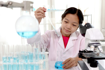 Adorable schoolgirl in lab coat doing science experiments, young scientist adding some chemical to blue flask with pipette and learning science experiment in laboratory. Asian kid using microscope, ap