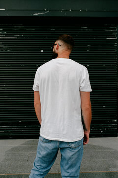 Young Bearded Hipster Guy Wearing White Blank T-shirt And Blue Jeans In A Random Urban Style. Design Men T Shirt Mock-up For Print