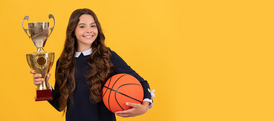 smiling kid hold basketball ball and champion cup on yellow background, achievement. Horizontal...