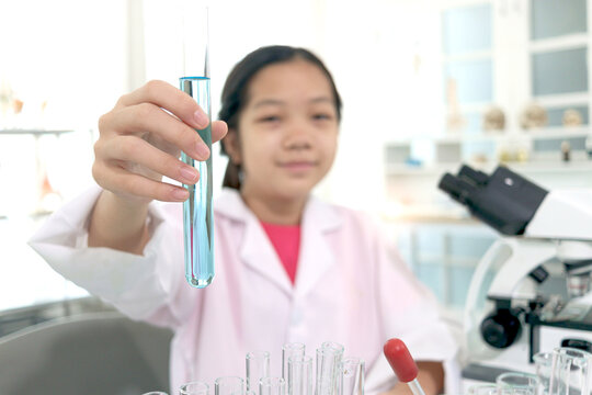 Hand of schoolgirl in lab coat showing blue chemical showing test tube to camera, kid doing science experiments, young scientist student learning science experiment in laboratory. Asian kid using micr
