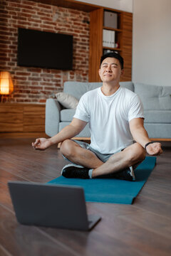 Peaceful Asian Mature Man Meditating With Closed Eyes In Front Of Laptop Computer At Home, In Living Room, Cropped