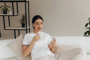 A woman is drinking coffee and using on a cell phone at home