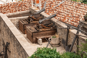 Naklejka premium an old rusty cannon with wooden wheels near a defensive stone wall. An old gun. Cannon with cores to protect the fortress. A historical monument.