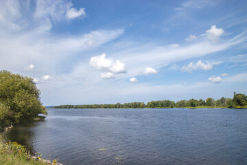 View across a wide river, trees on both shores, interesting cloud formation, blue sky, nobody
